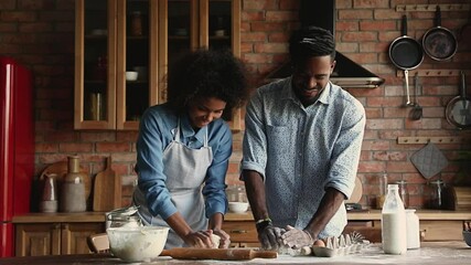 Wall Mural - Happy young family African wife and husband standing in cozy kitchen kneading dough cooking together prepare pastries for holiday dinner, celebrate event, enjoy romantic date and communication at home