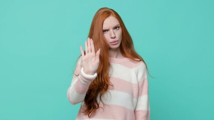 Wall Mural - Dissatisfied ginger redhead young girl in white pink sweater isolated on blue turquoise background studio. People lifestyle concept. Looking camera say no showing stop gesture with palm crossed hands