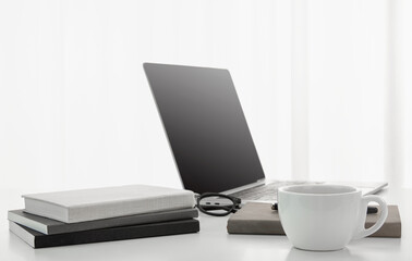 Wall Mural - Closeup of a cup of coffee, laptop, notebooks, and a pair of glasses on a white desk