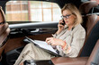 © pressmaster - Serious blond businesswoman sitting in taxi cab and calling business partner
