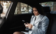© Liubov Levytska - Businesswoman travelling by car on backseat, reading text message on smartphone while driving on meeting