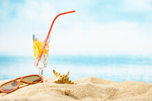 Closeup Of Refreshing Summer Drink With Lemons And Straw And Sunglasses On A Sandy Beach