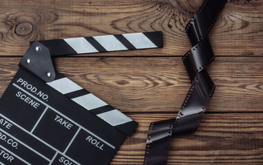 Film clapper board with film tape on wooden background. Cinema industry, entertainment. Top view