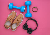 Fototapeta Sypialnia - Sports shoes, dumbbells and stereo headphones, smart bracelet on pink background. Getting ready for training. Top view. Flat lay