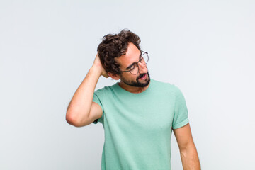 young bearded man smiling cheerfully and casually, taking hand to head with a positive, happy and confident look