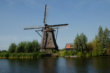 Wall Mural - Kinderdijk, The Netherlands, August 2019. On a beautiful summer day a historic windmill, in perfect condition, in the Dutch countryside furrowed by canals lined with tall green grasses.