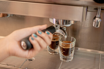 Barista serving coffee with a coffee maker in two small glasses