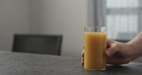 Slow motion ma hand take cold pressed orange juice in highball glass from concrete countertop with copy space