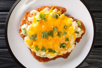 Fried chicken fillet baked with bechamel sauce and cheddar cheese close-up in a plate on the table. horizontal top view from above