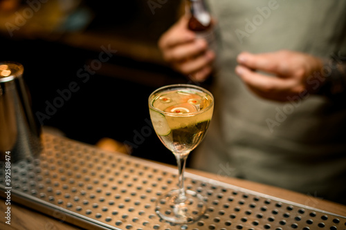 wine glass with drink decorated with slice of cucumber stands on bar counter surface