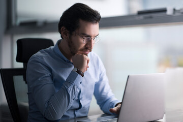 Authentic looking Turkish man concentrated thinking focused to his laptop and working in serious mood in a modern office, copy space.