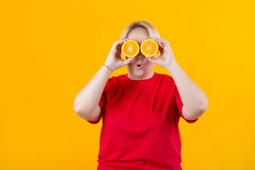 Wall Mural - beautiful young plump female in a red t-shirt on a yellow background with oranges