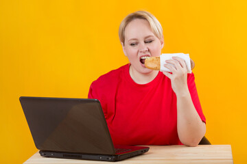 Wall Mural - beautiful young plump female in a red t-shirt on a yellow background with a laptop eating fast food