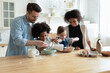 Happy diverse parents with kids preparing dough for cookies or pancakes in modern kitchen, African American mother and Caucasian father teaching kids to cook, multiracial family enjoying weekend