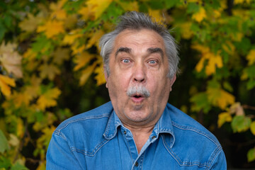 Portrait of 70-year-old elderly man, gesturing funny and comical, his expression looks cheerful.