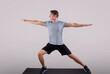 Handsome young man in sportswear doing warrior yoga pose on sports mat over light background, full length portrait