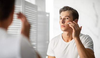 Confident man looking in the mirror applying cream on face