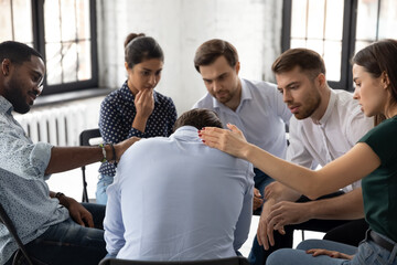 On group therapy session. Compassionate diverse multiethnic men and women gently touching shoulders of crying suffering male teammate sharing his personal problem expressing support care understanding