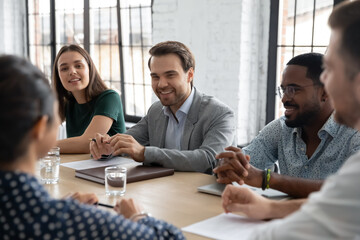 Wall Mural - Sharing ideas. Smiling confident multiethnic employees businesspeople colleagues gathered together at conference desk brainstorming discussing marketing strategy plan engaged in talks negotiations