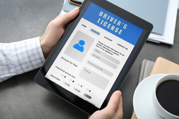 Man holding tablet with driver's license application form at grey table, closeup
