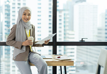 Asian Muslim businesswoman in hijab head scarf planing work with paper chart and computer laptop in the modern office. businesspeople, diversity and office concept