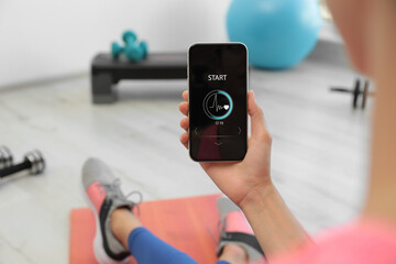 Young woman using fitness app on smartphone indoors, closeup