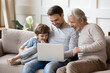 © fizkes - Smiling little boy with father and mature grandfather using laptop, sitting on couch, happy three generations of men looking at computer screen together, watching video, shopping or chatting online