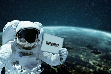 Wall Mural - astronaut in a space suit shows a card with the text welcome spacewalk against the background of the