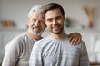 Head shot portrait smiling mature father and adult son hugging, standing, posing for photo at home, happy older grandfather and grandson looking at camera, two generations bonding concept