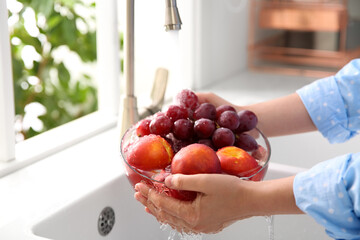 Wall Mural - Woman washing fresh grapes and nectarines in kitchen sink, closeup