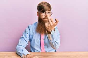 Canvas Print - Young irish redhead man wearing business shirt and tie sitting on the table showing middle finger, impolite and rude fuck off expression