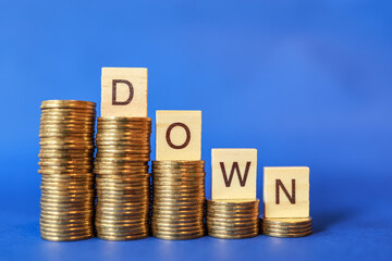 Business, Money and Finacial Concept. Closeup of English letter DOWN wooden block on top of stack of gold coins on blue background.