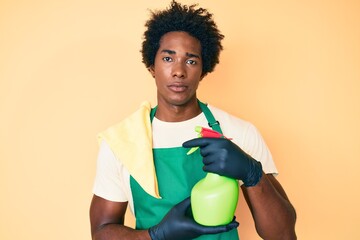 Poster - Handsome african american man with afro hair wearing apron holding cleaning spray thinking attitude and sober expression looking self confident