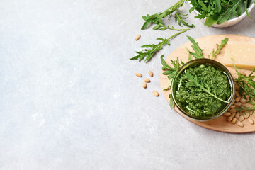 Bowl of tasty arugula pesto and ingredients on light table, flat lay. Space for text