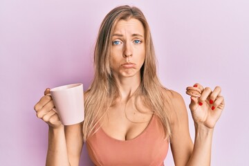 Poster - Beautiful caucasian woman drinking coffee and eating french pastry macaron depressed and worry for distress, crying angry and afraid. sad expression.