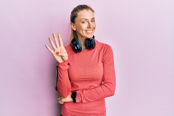 Sticker - Beautiful caucasian woman wearing sportswear and arm band showing and pointing up with fingers number four while smiling confident and happy.