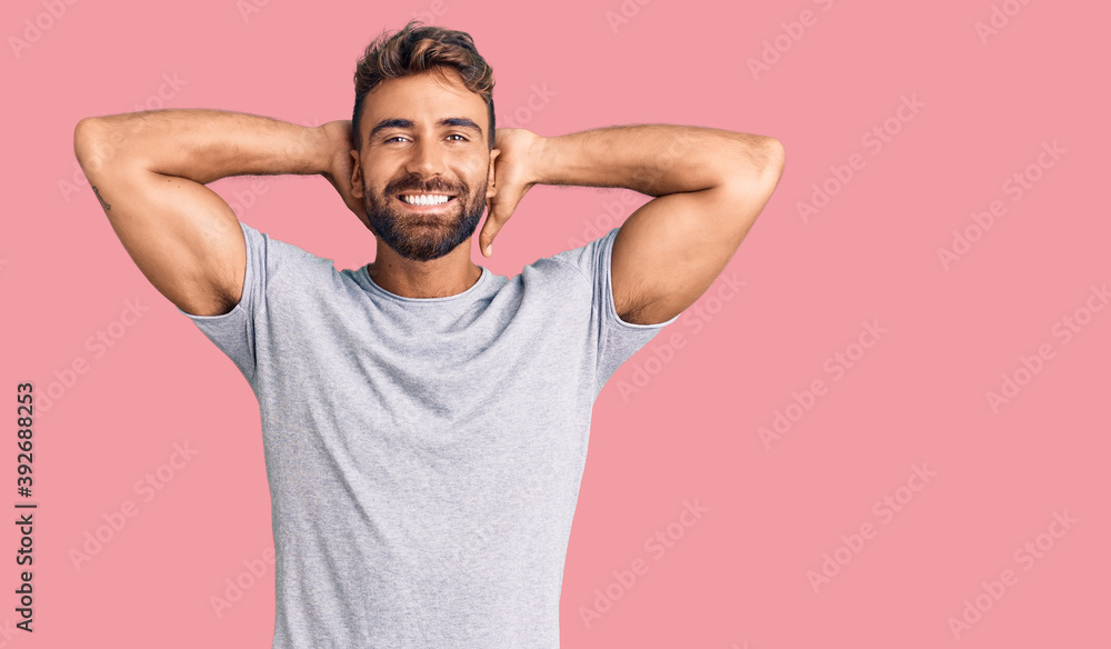 Young hispanic man wearing casual clothes relaxing and stretching, arms and hands behind head and neck smiling happy