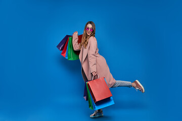 .Young blonde girl in a cardigan on a blue background with a shopping bag