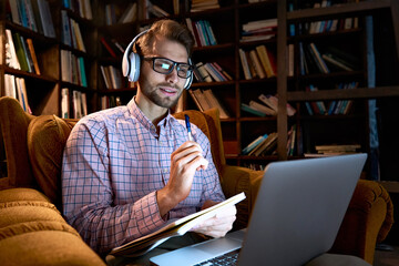 Wall Mural - Young business man, male student wearing headphones elearning on laptop computer sitting in chair working from home office, learning online, studying remote training course, watching webinar stream.