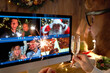 © insta_photos - Young man wears Christmas hat drinking champagne holding sparkler talking to friends on virtual video call celebrate Happy New Year party in distance online chat at home, over shoulder screen view.