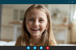 © fizkes - Close up head shot adorable little happy caucasian girl looking at web camera, enjoying online video call conversation with friends or attending distant educational class, e-learning alone at home.