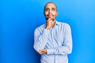 Poster - Hispanic adult man wearing business shirt over blue background thinking concentrated about doubt with finger on chin and looking up wondering