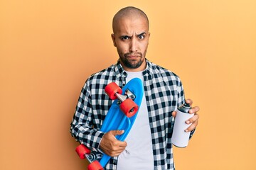 Poster - Hispanic adult skater man holding skate and graffiti spray skeptic and nervous, frowning upset because of problem. negative person.