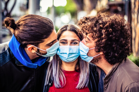 Double kiss with medical protective mask on face for fear of virus infection - Young millennials friends wearing protective face masks and kissing each other on the cheek 