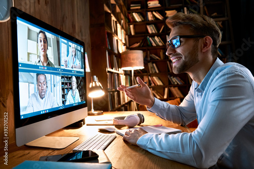 Obraz Dibond Business man having virtual team meeting on video conference call using computer. Social distance worker working from home office talking to diverse colleagues in remote videoconference online chat.
