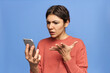 © Anatoliy Karlyuk - Frustrated young female expressing indignation, gesturing emotionally while reading shocking news on internet via cell phone. Irritated frowning woman receiving unpleasant weird text message on mobile