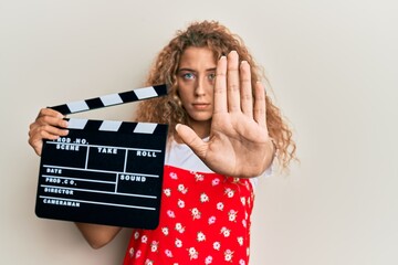 Sticker - Beautiful caucasian teenager girl holding video film clapboard with open hand doing stop sign with serious and confident expression, defense gesture