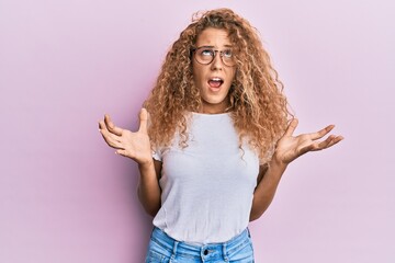 Beautiful caucasian teenager girl wearing white t-shirt over pink background crazy and mad shouting and yelling with aggressive expression and arms raised. frustration concept.