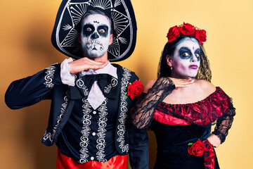 Poster - Young couple wearing mexican day of the dead costume over yellow cutting throat with hand as knife, threaten aggression with furious violence