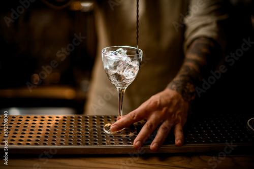close-up of glass with ice cubes being stirred by bartender with long bar spoon